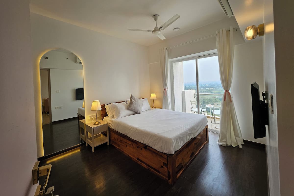 A bedroom with a wooden bed, a ceiling fan, a nightstand with a lamp, a large mirror, and a view of the outdoors through a sliding glass door.