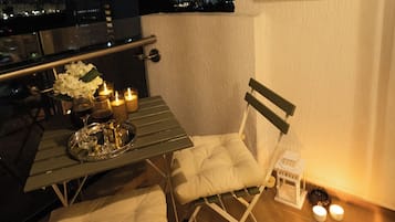 A balcony with a table set for two, a chair, and a view of the cityscape at night.