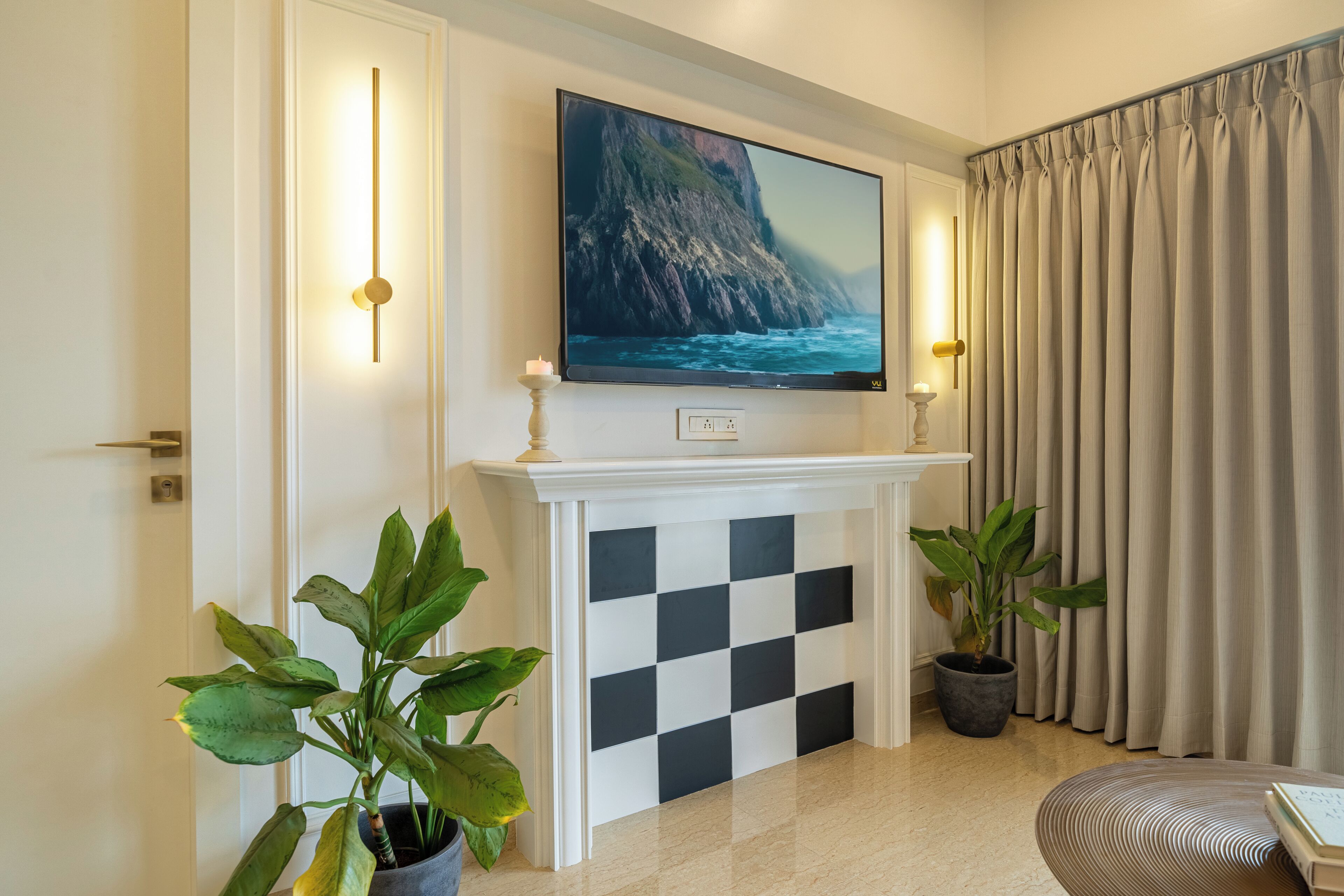 Ein Zimmer mit Kamin, einem darüber angebrachten Fernseher und zwei Blumentöpfen.
