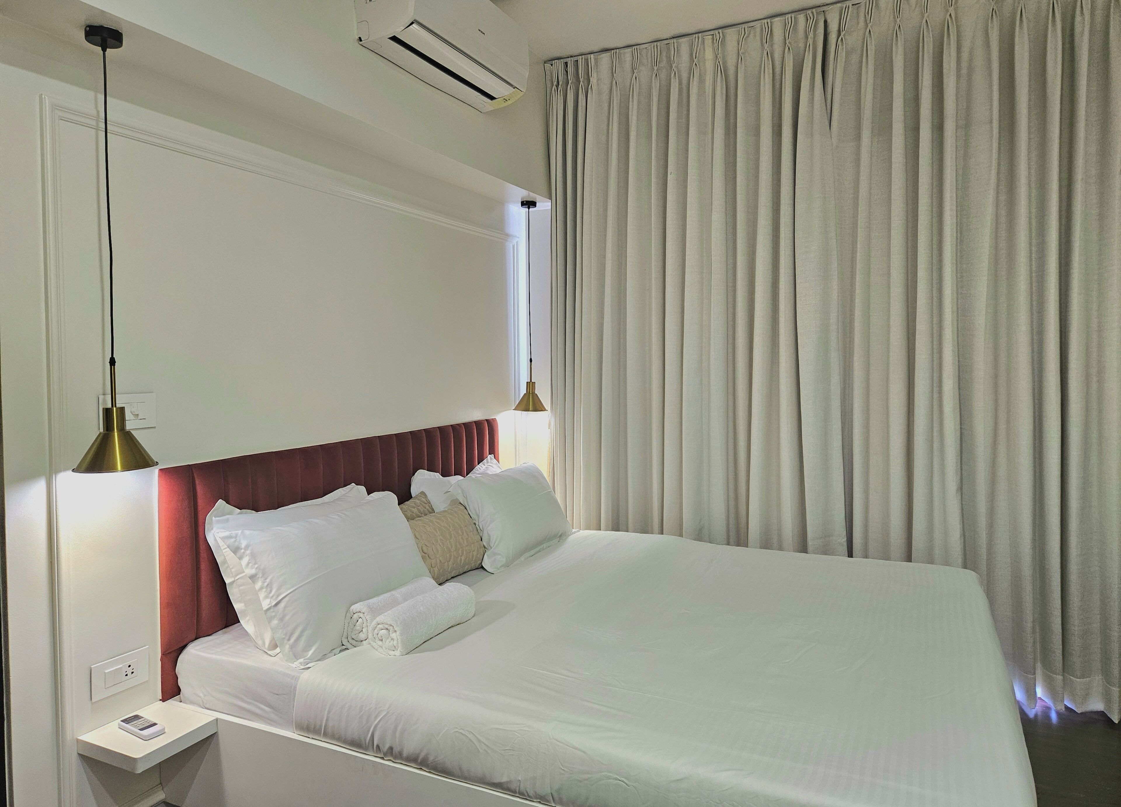 Een hotelkamer met een groot bed, twee bedlampen, een nachtkastje en een raam met gordijnen.