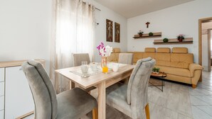 Ein Essbereich mit einem Holztisch, grau gepolsterten Stühlen und einem beigefarbenen Sofa im Hintergrund.