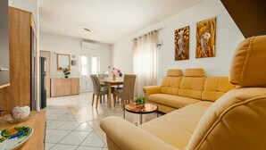 Ein modernes Wohnzimmer mit einer Couch, einem Essbereich mit Stühlen, einer Küche mit Schränken und einem großen Fenster mit Vorhängen.