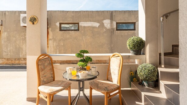 Ein Balkon mit zwei Stühlen, einem kleinen Tisch, einem Bonsai-Baum und einem Blumentopf.