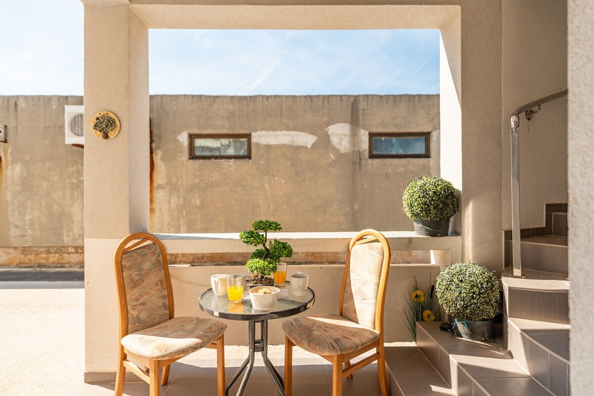 Ein Balkon mit zwei Stühlen, einem kleinen Tisch, einem Bonsai-Baum und einem Blumentopf.