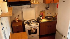 Een kleine keuken met een gasfornuis, oven, spoelbak en een koelkast.