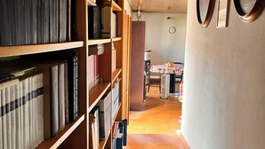 Een gang met houten boekenkasten vol boeken, een betegelde vloer en een eethoek in de achtergrond.