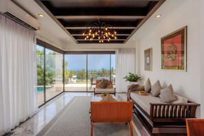 A spacious room with a large sliding glass door leading to a balcony, a wooden sofa, a dining table, and a modern chandelier. - ediResidences Family Pool Villa w/ Ocean View (Koh Samui)