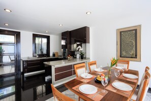 A modern kitchen with dark cabinetry, a central island, and a dining area with a wooden table set for four. - ediResidences Family Pool Villa w/ Ocean View (Koh Samui)