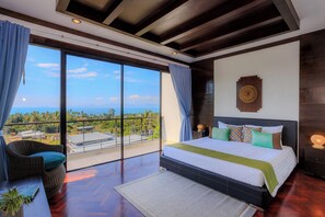 A bedroom with a large bed, a view of the sky and landscape, a wicker chair, and a nightstand with a lamp. - ediResidences Family Pool Villa w/ Ocean View (Koh Samui)