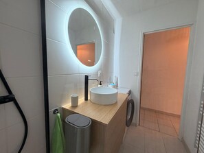 A modern bathroom with a round mirror, a sink, and a toilet. - Apartment with AC, parking - 4 guests (Banyuls-sur-Mer)