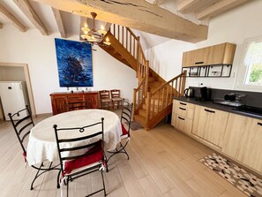 A dining area with a round table, chairs, and a staircase leading to a kitchen. - Authentic gîte with garden - 4 guests (Thésée)