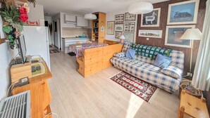 Uma sala de estar aconchegante, com um sofá de madeira, uma mesa de jantar e uma cozinha ao fundo.