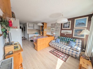 Un salon chaleureux avec un canapé en bois, une table à manger et une cuisine en arrière-plan.