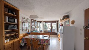 Cozinha compacta com armários de madeira, uma mesa de jantar com cadeiras, um refrigerador e vista pela janela.