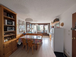 Une cuisine compacte avec des meubles en bois, une table à manger avec des chaises, un réfrigérateur et une vue par la fenêtre.