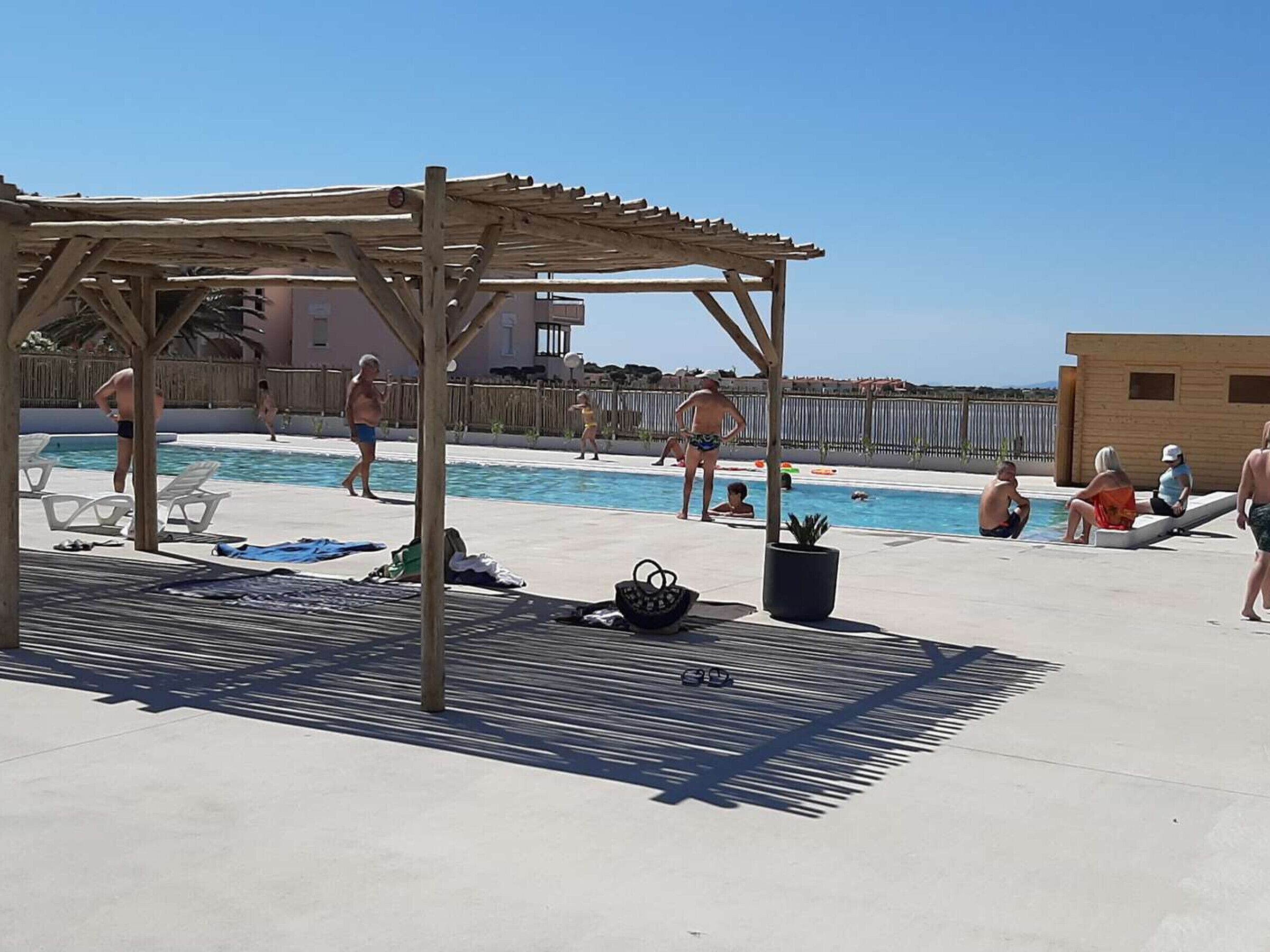 A pool area with a pergola, lounge chairs, and a clear sky.