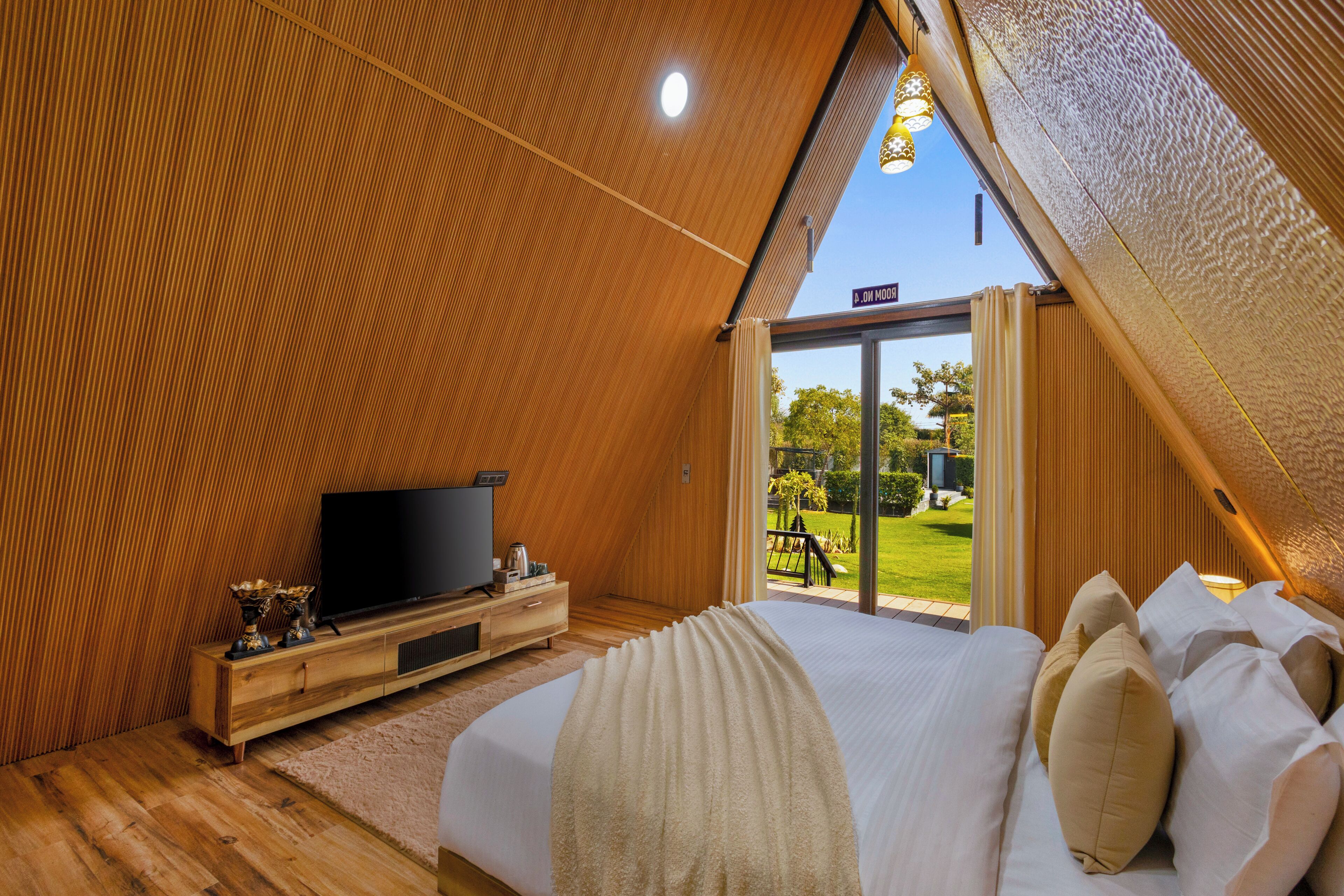 A bedroom with a large bed, a TV, wooden paneling, and a view of the outdoors.