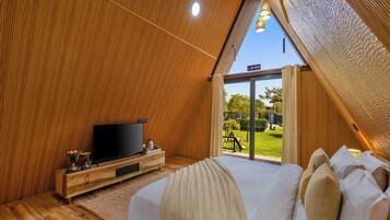 A bedroom with a large bed, a TV, wooden paneling, and a view of the outdoors.