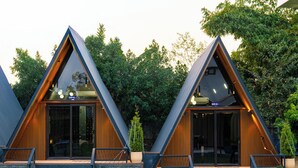 Twee moderne, driehoekige gebouwen met grote ramen, houten details en een stenen fundering.