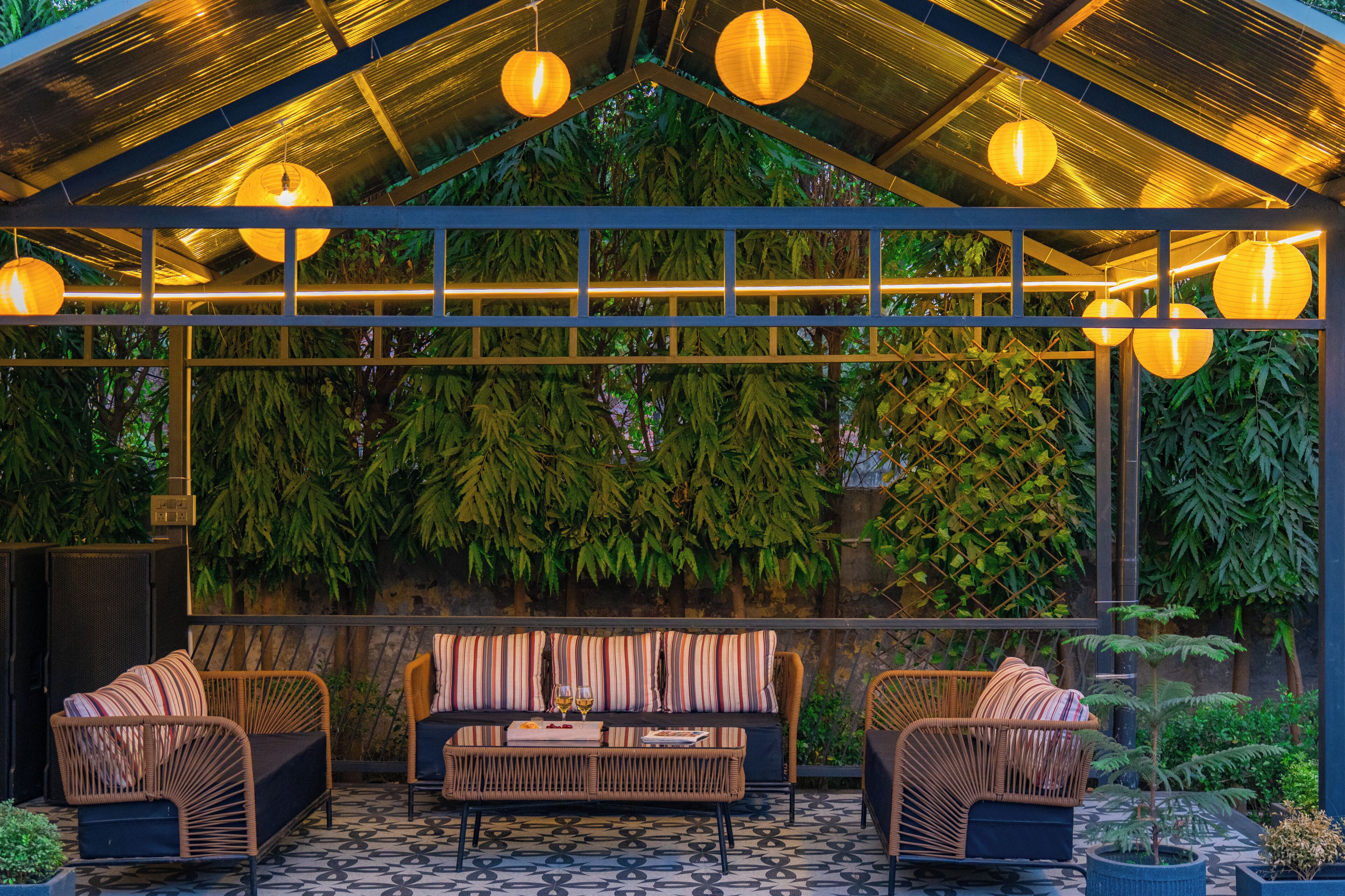 A covered outdoor seating area with a patterned floor, cushioned chairs, a sofa, and hanging lanterns.