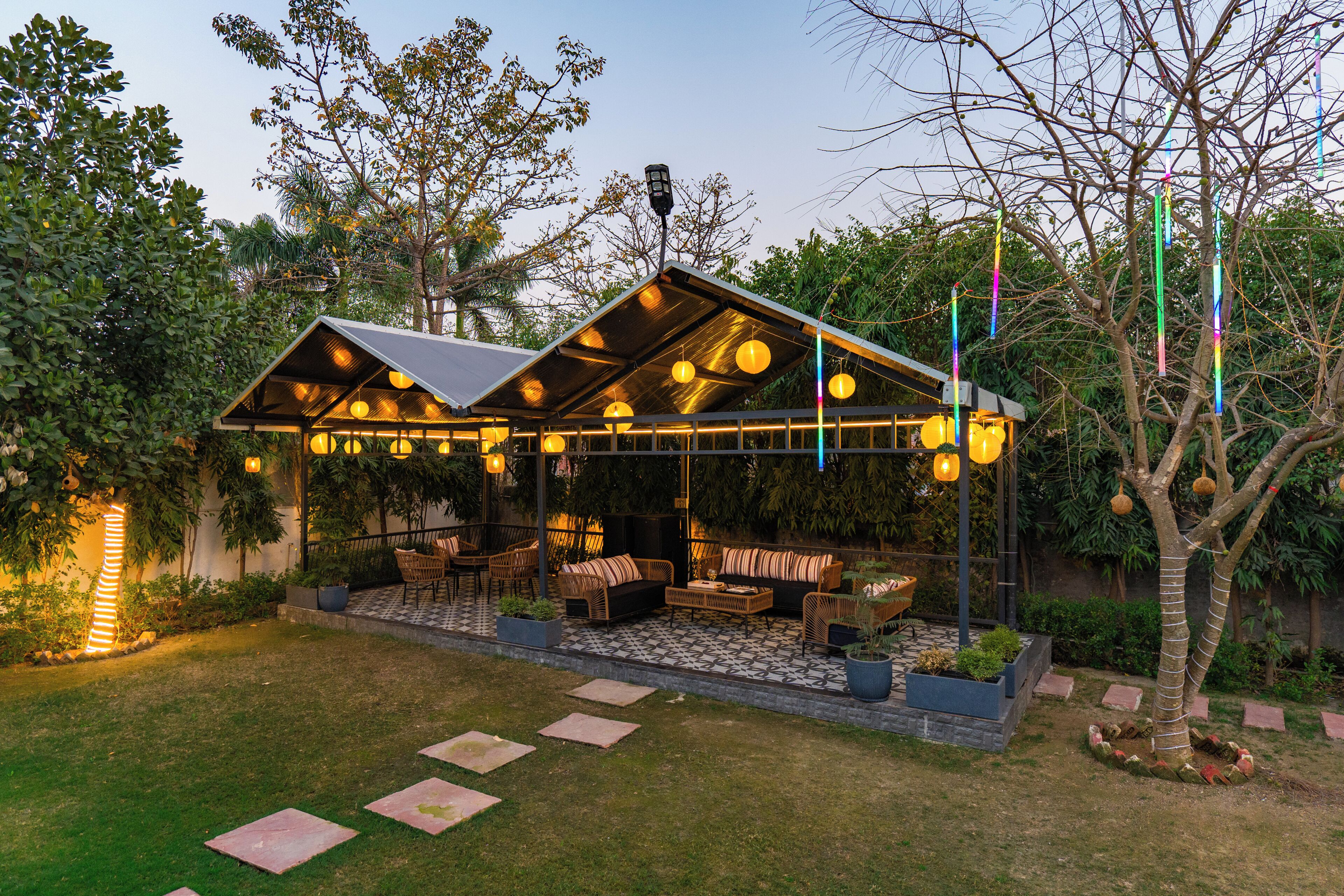 A covered outdoor seating area with tables and chairs, surrounded by greenery.