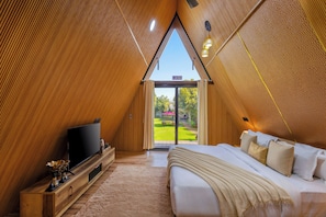 Un dormitorio con cama, televisor y vista a un jardín a través de un ventanal.