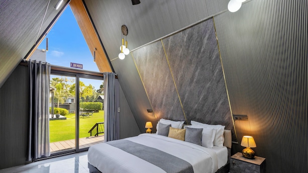 Een moderne slaapkamer met een groot bed, een nachtkastje met een lamp en uitzicht op een tuin door een schuifdeur.