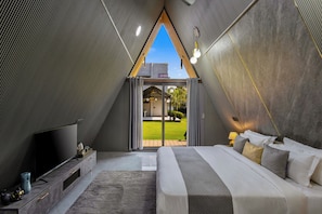 Un dormitorio moderno con una cama grande, un televisor de pantalla plana y vistas a un jardín verde a través de un ventanal.