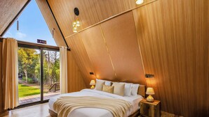 Een slaapkamer met een groot bed, een nachtkastje, een lamp en uitzicht op een tuin door een glazen deur.