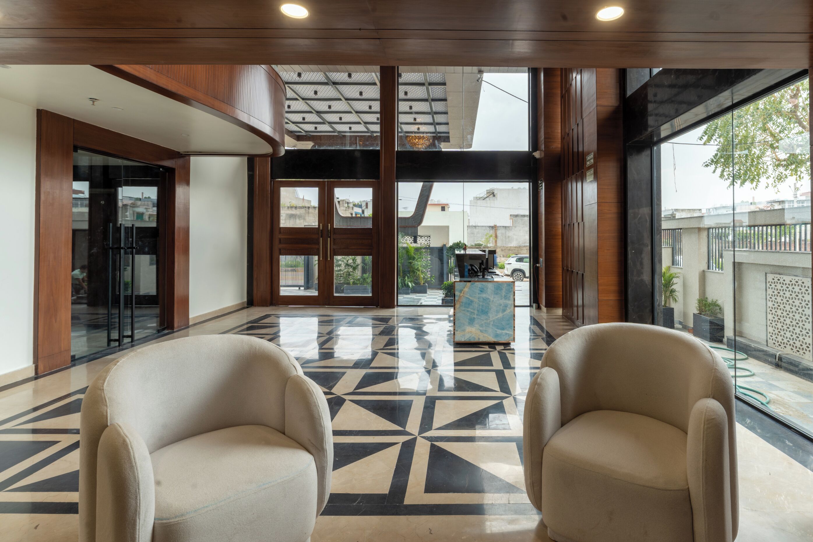 Un hall con dos sillones color beige, un suelo con estampado geométrico y vistas al exterior a través de amplios ventanales.