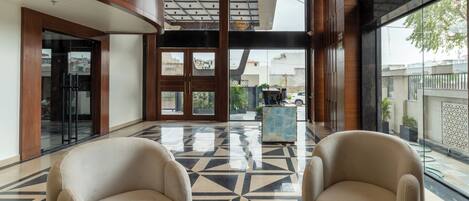 Un hall con dos sillones color beige, un suelo con estampado geométrico y vistas al exterior a través de amplios ventanales.