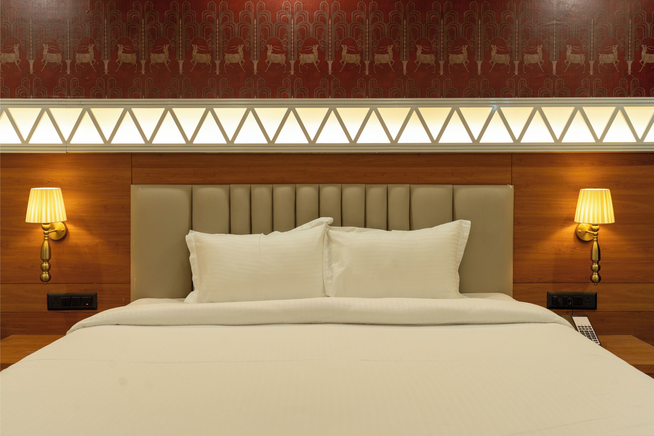A hotel room with a large bed, two bedside lamps, a patterned wall, and a wooden headboard.