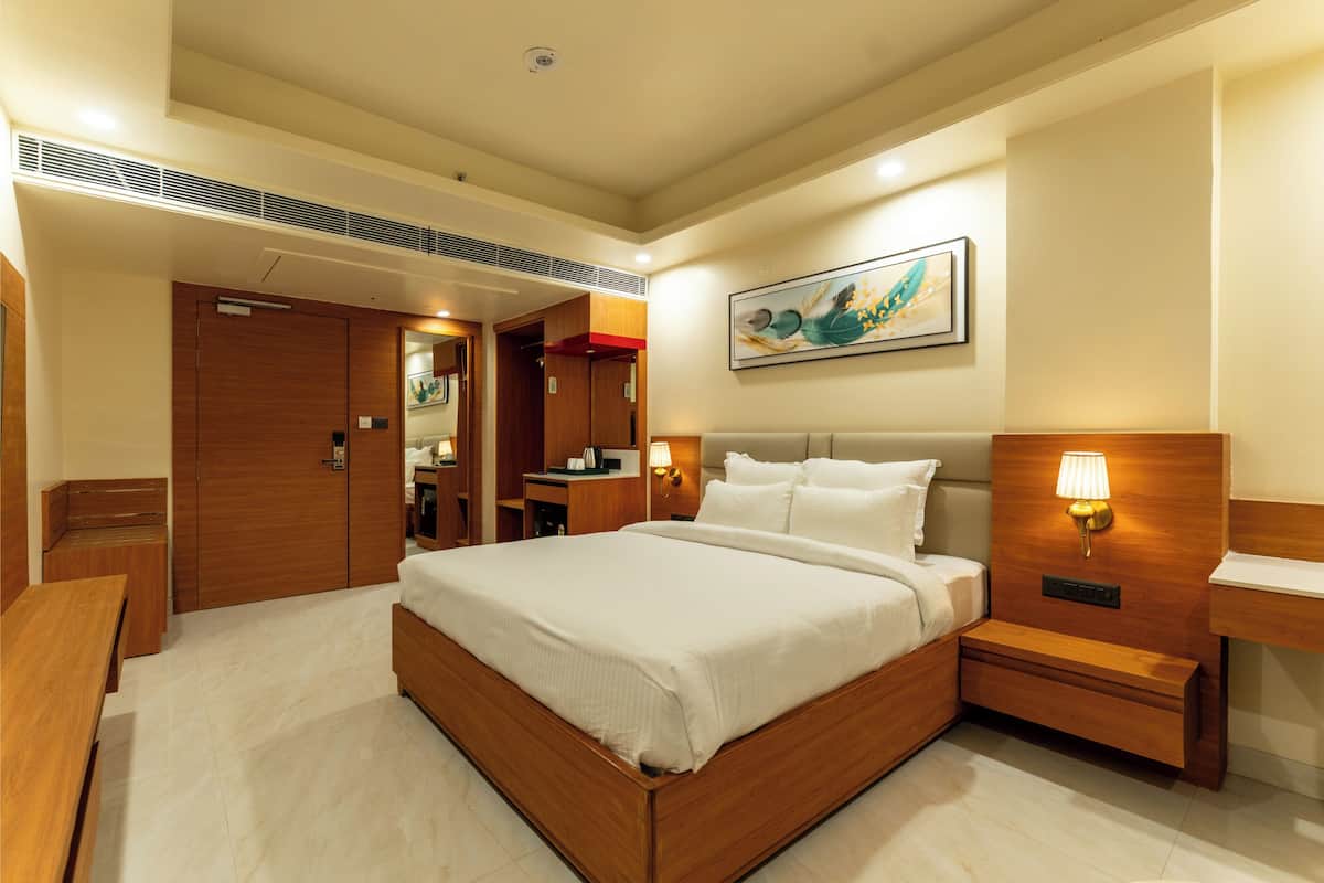 A hotel room with a large bed, bedside tables, a desk, a mirror, and a painting on the wall.