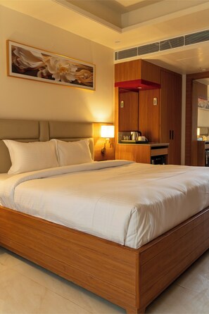 A large bed with a wooden frame, a nightstand with a lamp, and a painting on the wall. - Innara - A Boutique Luxury Hotel (Jaipur)