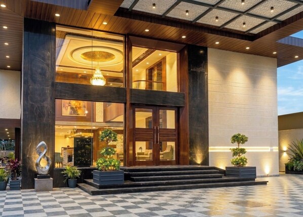 A modern hotel entrance with a checkered floor, a large chandelier, and a glass facade.