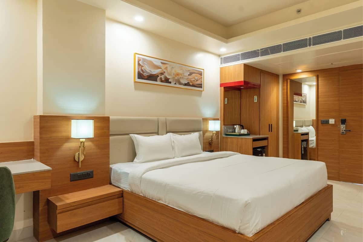 A modern hotel room with a large bed, bedside tables, a mirror, and a wooden wardrobe.