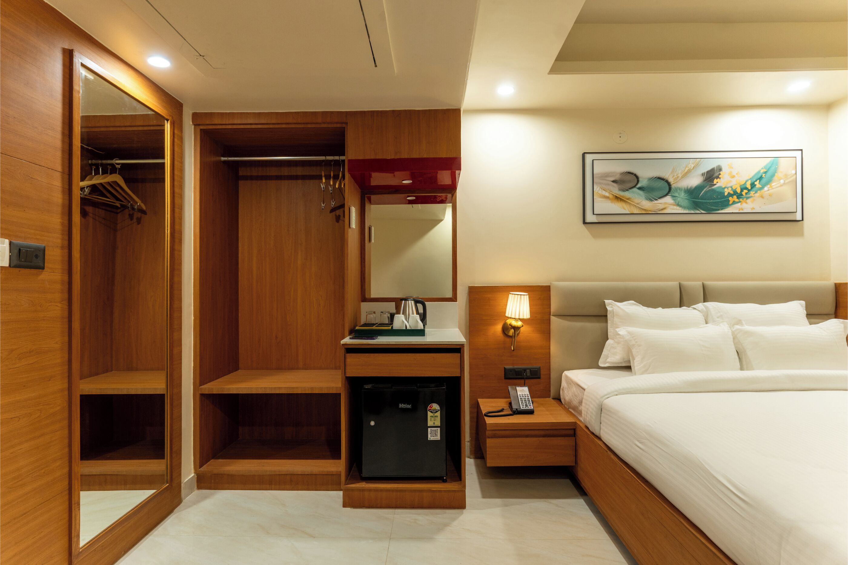 Une chambre d’hôtel comprenant un lit, un bureau avec une lampe, un mini-réfrigérateur, une armoire et un miroir.