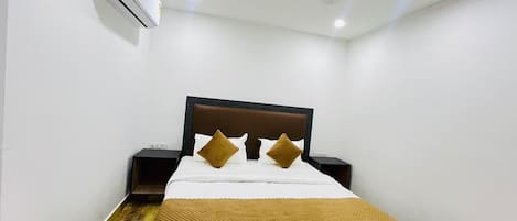 A hotel room with a bed, a ceiling fan, an air conditioning unit, and a nightstand.