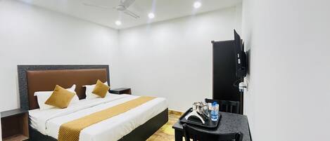 Ein Hotelzimmer mit einem Bett, einem Schreibtisch mit Stuhl, einem Fernseher und einem Deckenventilator.