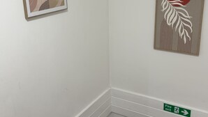 A corner of a room with a framed abstract artwork, a fire exit sign, and a wooden chair. - Two bedrooms house with a work space (Basildon)