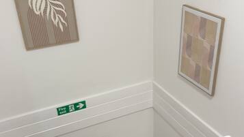 Eine Treppe mit hölzernen Geländern, einem Feuerschutzschild und zwei gerahmten Kunstwerken an den Wänden.