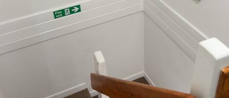 A staircase with wooden handrails, a fire exit sign, and two framed artworks on the walls.