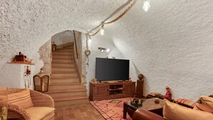 Une pièce chaleureuse, dotée d'un téléviseur, de meubles en osier, d'un escalier et d'un plafond rustique.