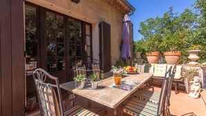 Une terrasse extérieure avec une table en bois, des chaises à rayures, des plantes en pot et une statue en pierre.