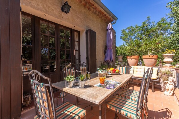 An outdoor patio with a wooden table, striped chairs, potted plants, and a stone statue.