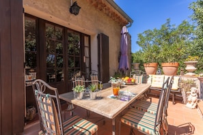 Eine AuĂenpatio mit einem Holztisch, StreifenstĂŒhlen, Topfpflanzen und einer Steinstatue.