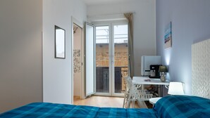 Una stanza con un letto, una scrivania, una sedia, un tavolo e un balcone con un muro in pietra.