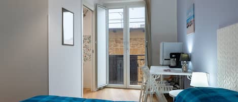 A room with a bed, a desk, a chair, a table, and a balcony with a stone wall.