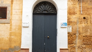 Une porte bleu foncé avec une poignée de porte en laiton, une fenêtre en arc blanc au-dessus et un socle en briques.