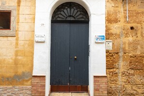A dark blue door with a brass doorknob, a white arched window above it, and a brick base. - Room 'Donna Letizia - Triple' with Balcony, Wi-Fi and Air Conditioning (Agrigento)